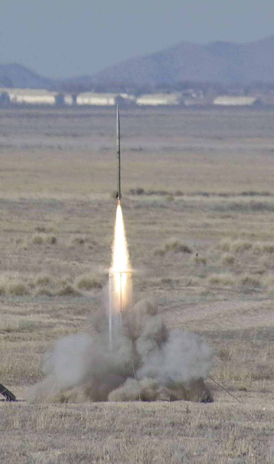 Personality leaving the pad, a very slender minimum-diameter airframe on a bright flame above the exhaust cloud.