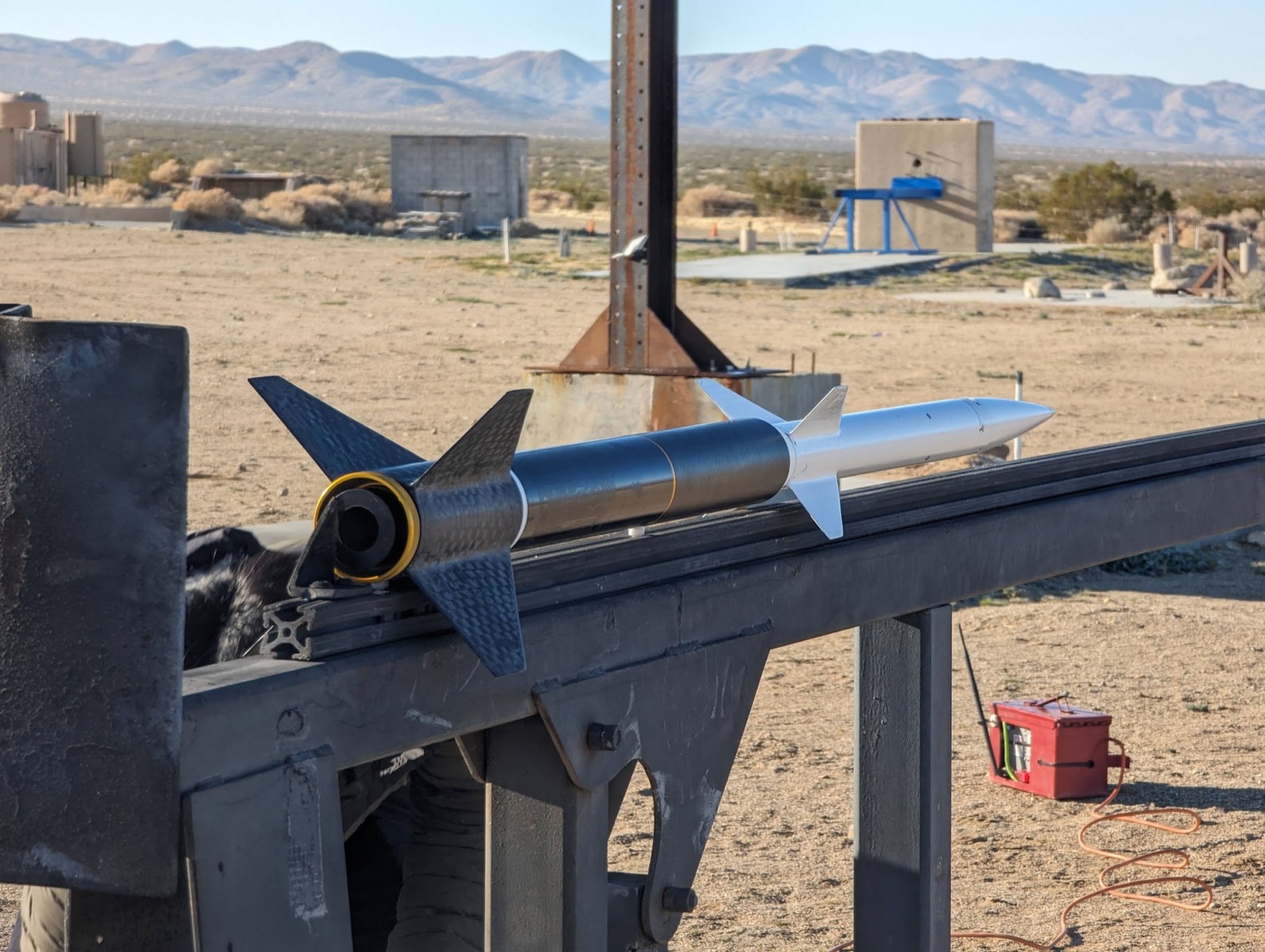 Project Streak fully integrated on the launch rail: carbon fiber booster with four swept fins, white sustainer and nosecone above it.