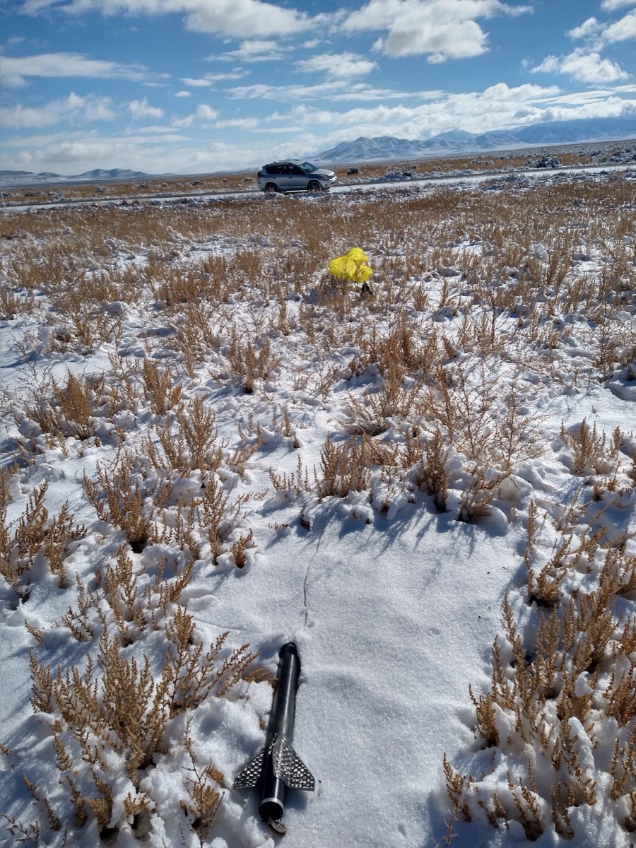 The carbon fiber sustainer lying in snow-covered scrub, its yellow parachute still inflated a few metres away.