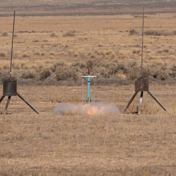 Up, Up, and Away at the moment of ignition between two launch towers, exhaust spreading across the ground.